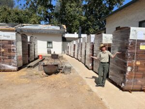 State Park Employee stands next to pallet of shingles. Rows of shingles in background. 