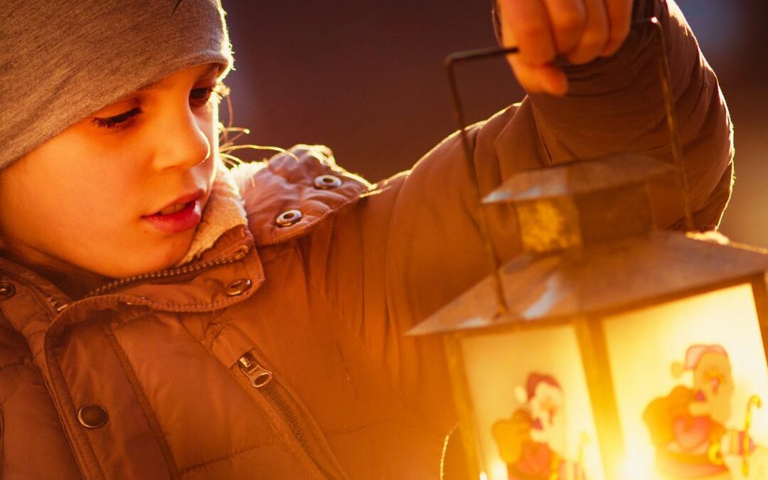 a child wearing a beanie holds a glowing lantern
